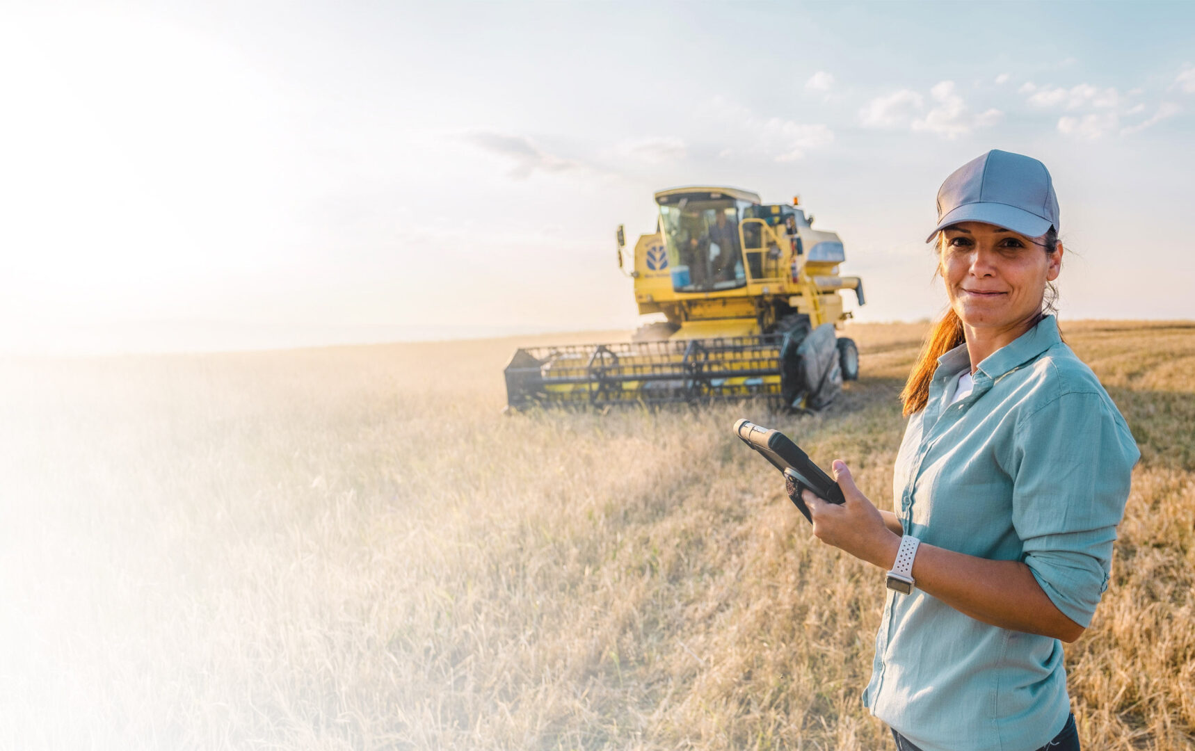 Farmer holding cellular connected mobile device standing in front of a large industrial harvester